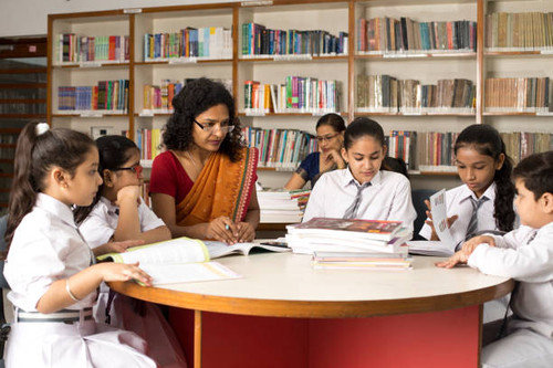 Female teachers teaching students in library at school.jpg