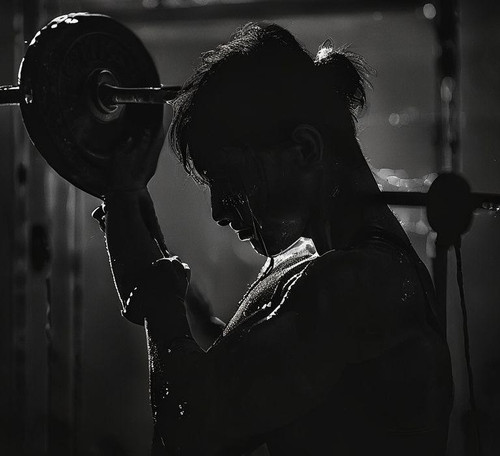 an individual lifts a heavy weight in a dimly lit gym sweat glistening on their brow as they focus.jpg