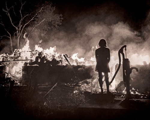 Silhouetted young woman looking at rural house fire, ca. 1960s