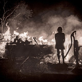 Silhouetted young woman looking at rural house fire, ca. 1960s