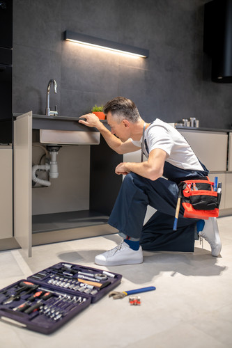 man kneeling down touching sink inspecting pipes.jpg