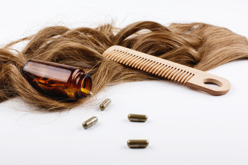 Wooden hair comb and bottle with vitamins lie on brown hair curls.jpg