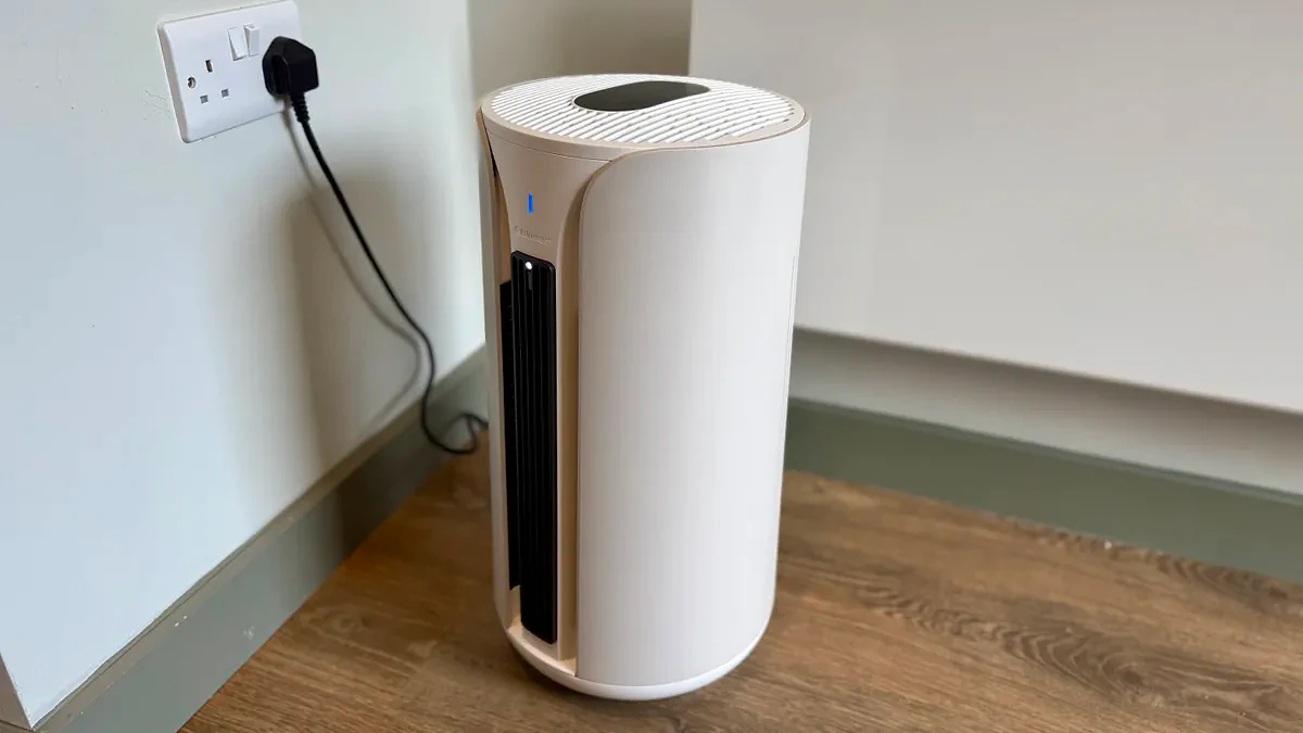 A photo of the Blueair T20i Air Purifier with its remote in a room with white walls and laminated wooden floors