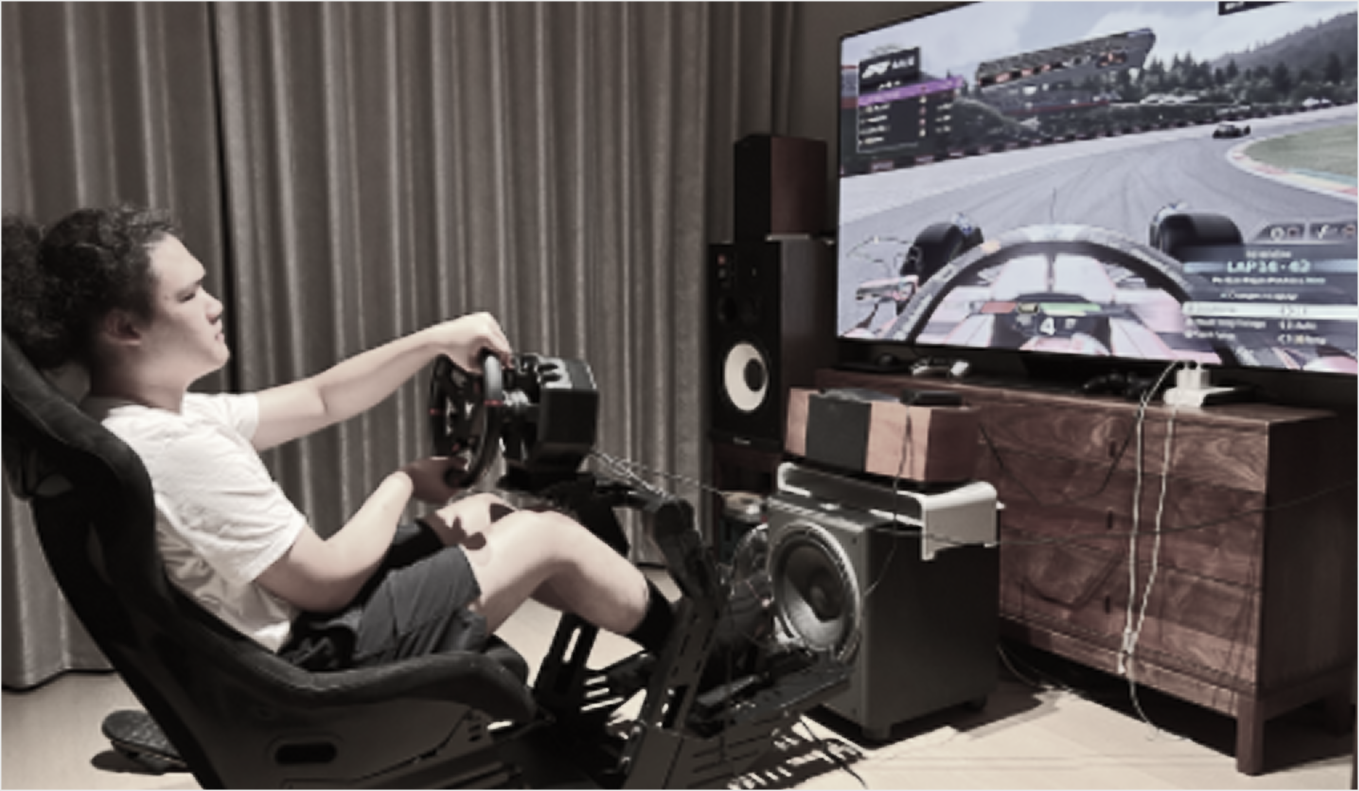 Driver in a home racing cockpit facing a large screen showing a race track
