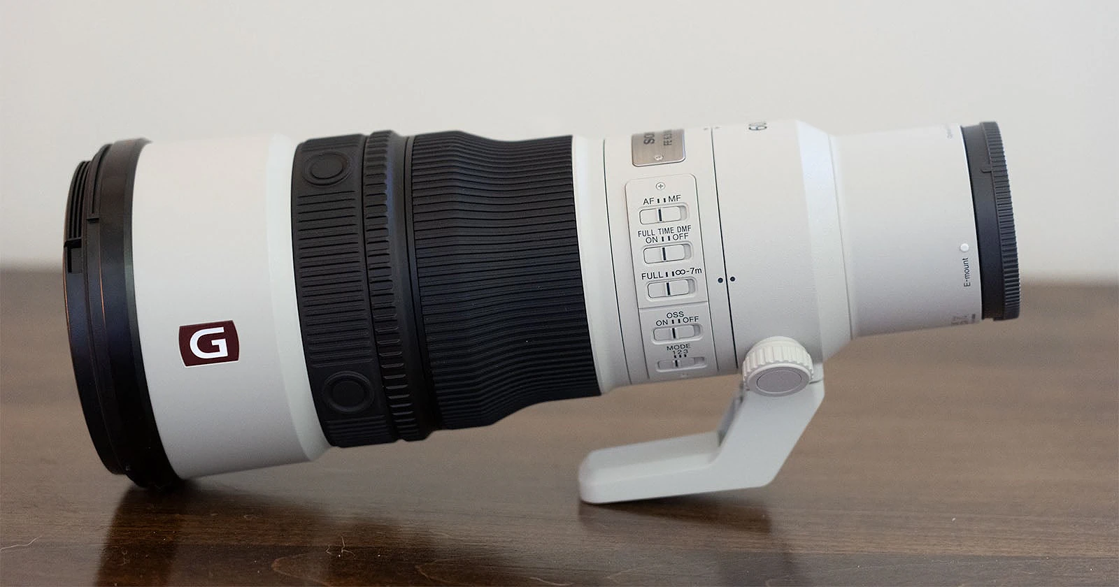 A white Sony FE 600mm f/4 GM OSS telephoto lens sits horizontally on a wooden surface, showing its side control panel and G-Master logo.