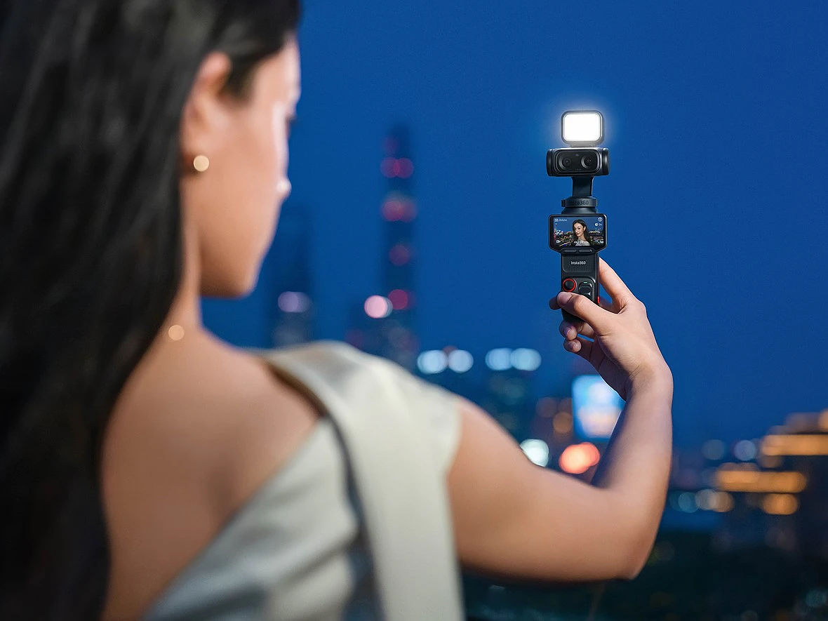 a woman holds a small camera gimbal with light at arms reach with a city nightscape behind