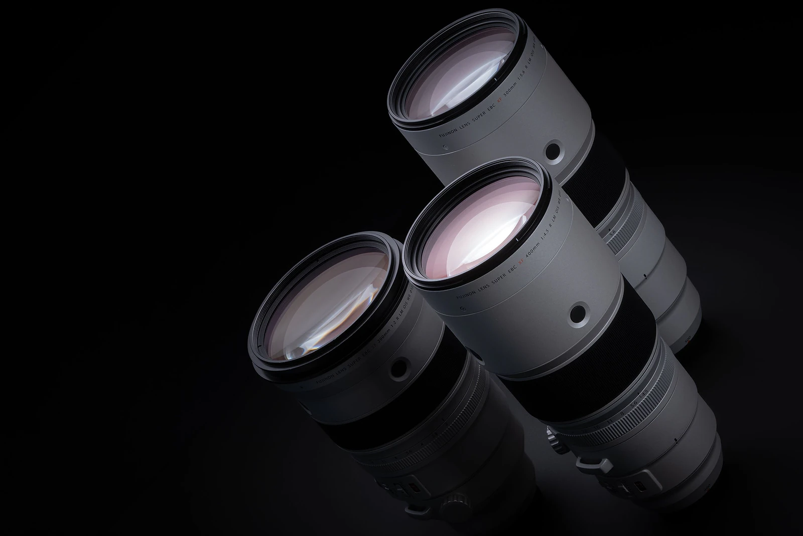Three silver telephoto camera lenses are arranged diagonally against a black background.