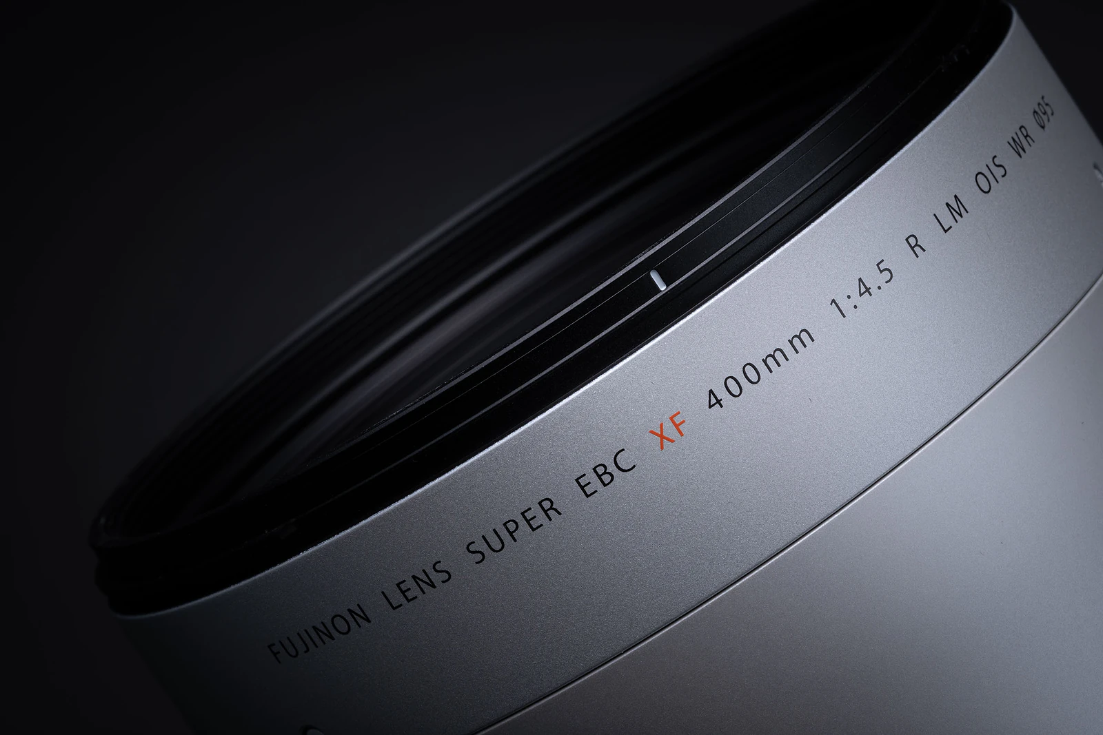 A close-up, angled view of a silver camera lens barrel against a dark background, showing the text "FUJINON LENS SUPER EBC XF 400mm 1:4.5 R LM OIS WR 095".