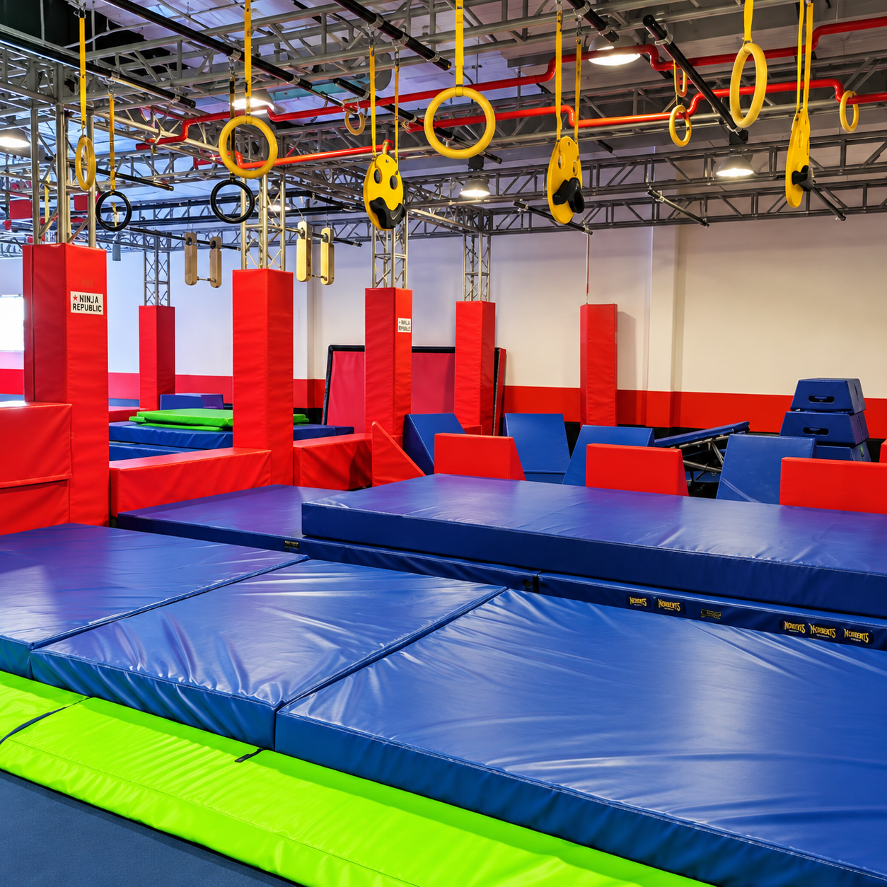 Indoor ninja course at Ninja Republic with hanging rings, red-padded towers, and blue mats