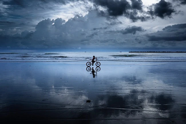A boy is riding his bicycle at a beach at low tide on Panay Island.