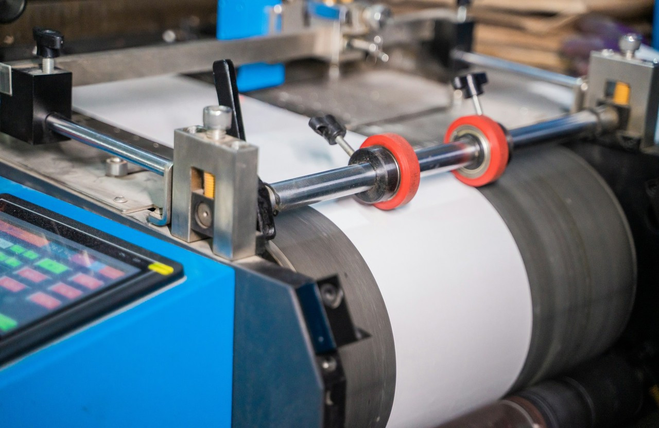 Rollenrotations-Flexodruckmaschine mit einem weißen Substrat, das über einen großen Gegendruckzylinder und rote Quetschwalzen läuft
