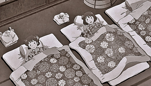 Zwei junge Mädchen in Blumenmuster-Kimonos liegen eingekuschelt in Futons auf dem Boden eines traditionellen Zimmers und blicken neugierig nach oben – dargestellt in weichen Sepiatönen mit gefalteten Kleidern und einem hölzernen Bottich in der Nähe.