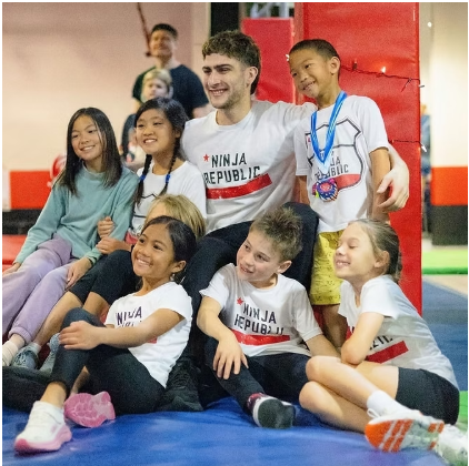 Young athletes and a young adult in Ninja Republic shirts gathered on the mats for a group photo