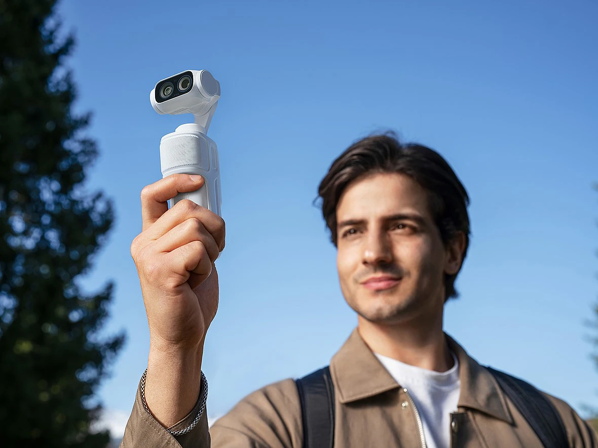 a man holds a white camera fimbal up with clear sky behind him