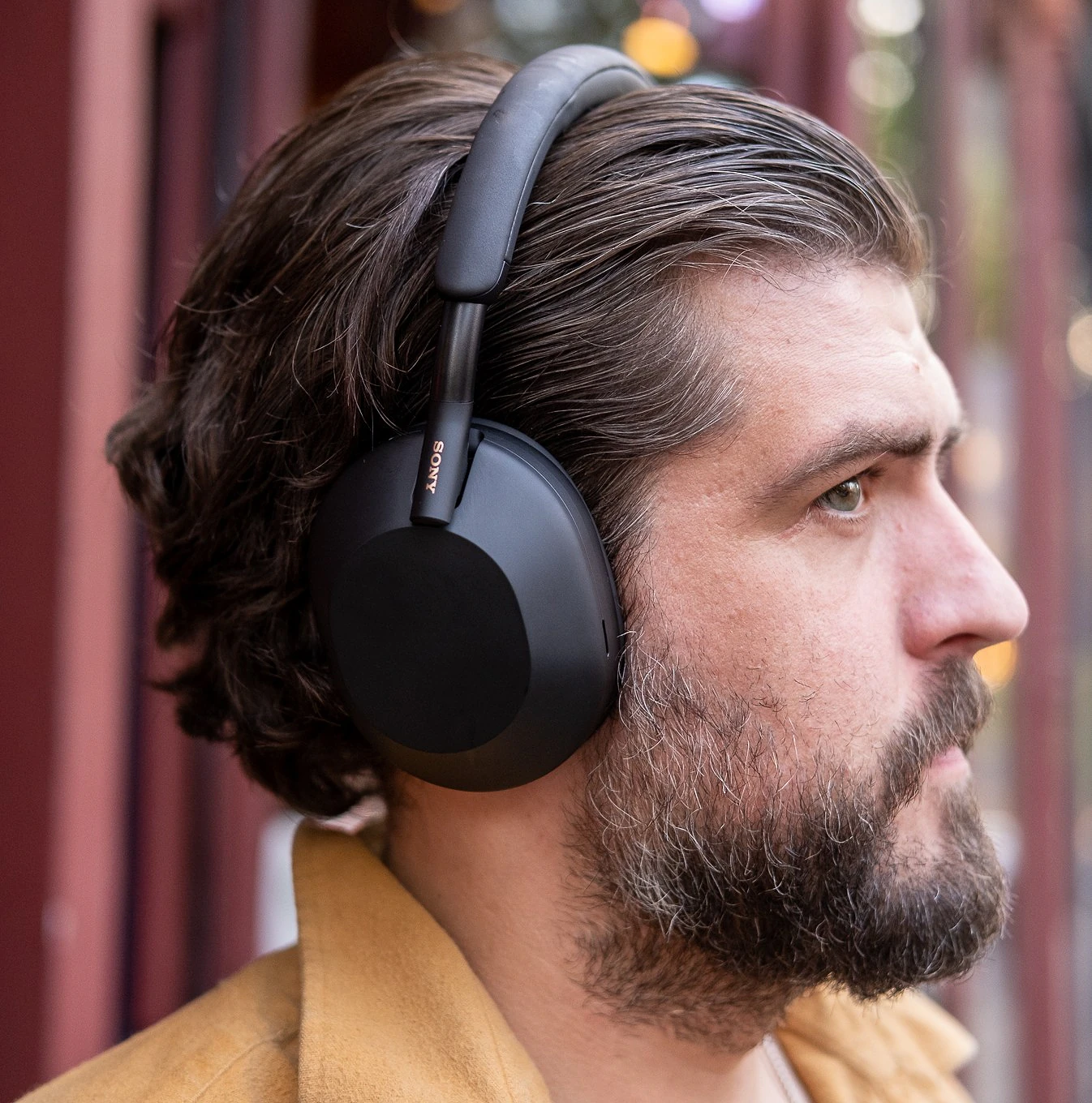 A man wearing Sony’s black WH-1000XM5 noise-canceling headphones outside.