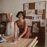 Cheerful young fashion designer in linen red dress smiles sincerely. Charming woman holds pencils an