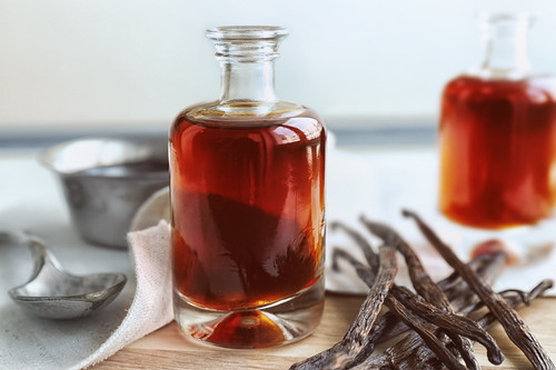 Bottle with aromatic extract and dry vanilla beans on table.jpg