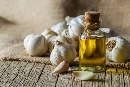 Ripe and raw garlic and garlic oil in glass of bottle on wooden table with burlap sack, alternative .jpg