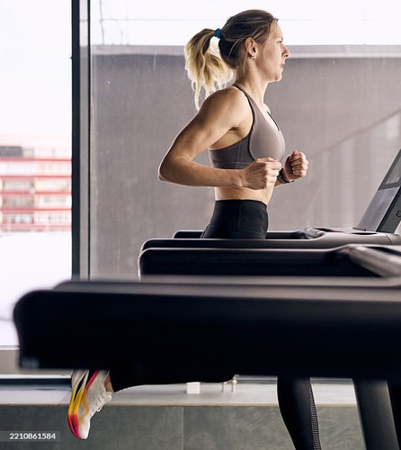 Side view of a fit woman running on a treadmill in a bright, modern gym. She appears focused and ene.jpg