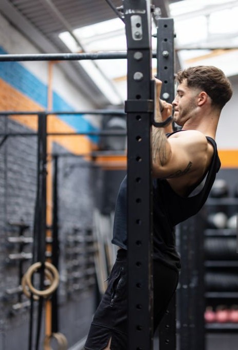 Side view of fit young man doing chin-ups on a bar at fitness studio. Male exercising in a cross tra.jpg
