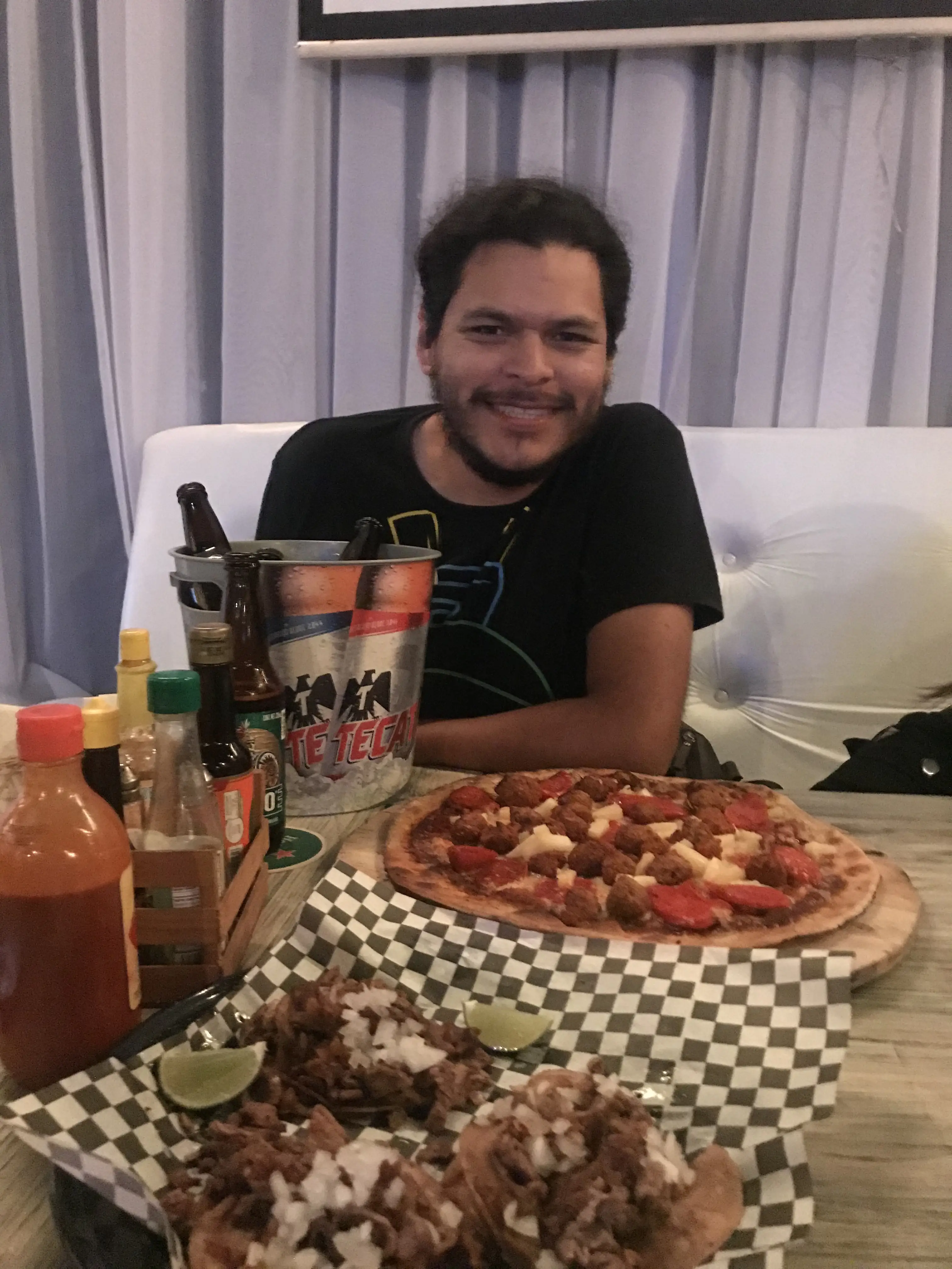 Daniel posando en la mesa servida con pizza hecha a mano, tacos y cubo de cervezas indio