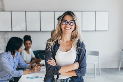 Pleased female secretary in trendy glasses posing in office after meeting with colleagues. Indoor po.jpg